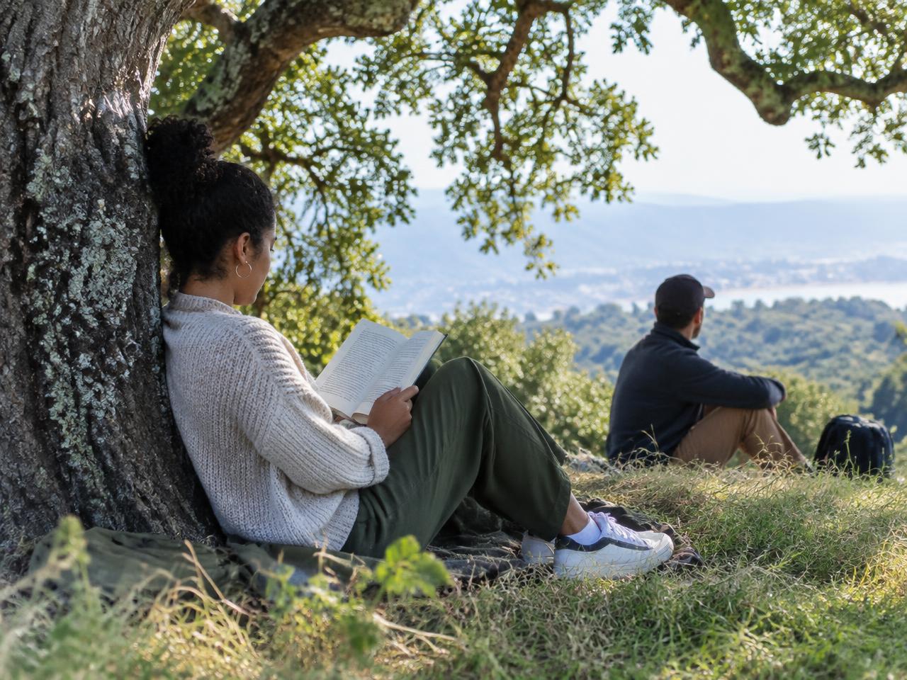 An adult reading outdoors beneath an oak tree